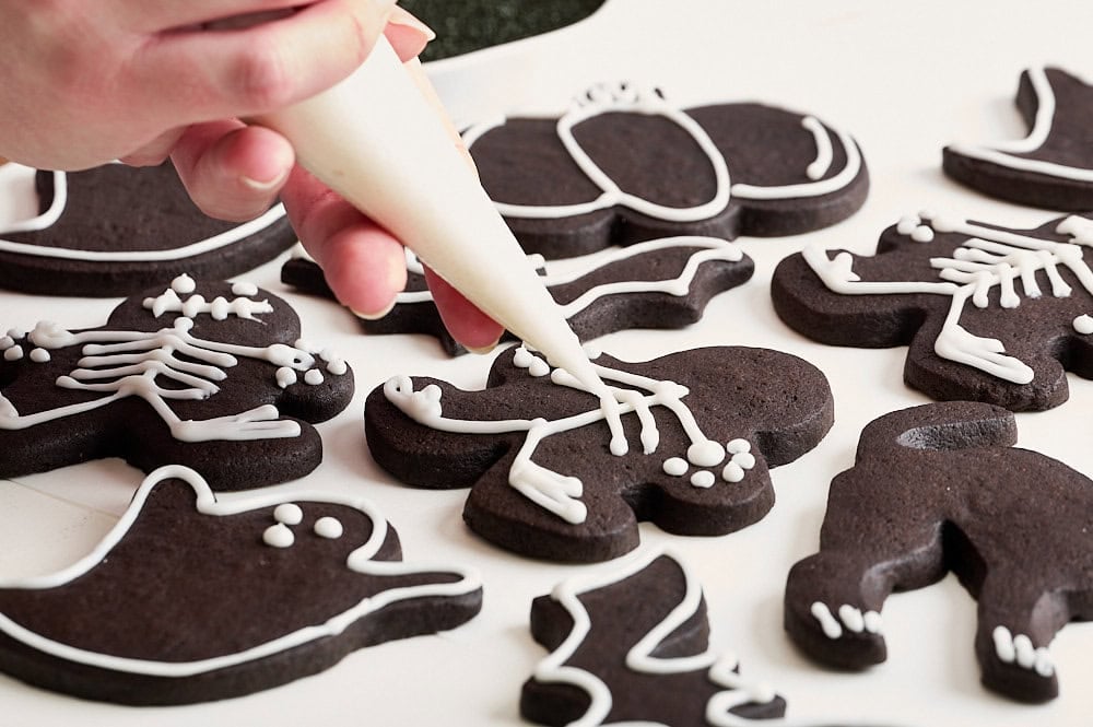 three quarter angle of black cocoa Halloween sugar cookies being iced with white border icing