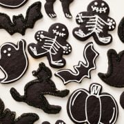 overhead view of many black cocoa Halloween sugar cookies decorated into various shapes including skeletons, ghosts, pumpkins, bats, and cats