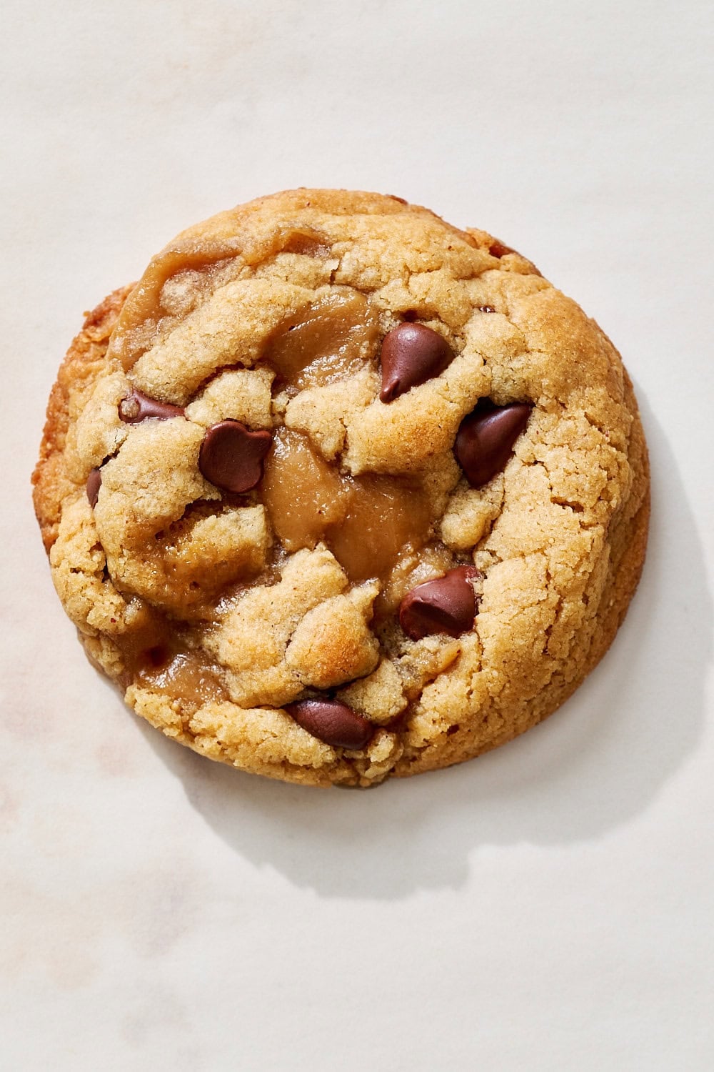 overhead view of one thick and chewy peanut butter toffee chocolate chip cookie on a marble counter